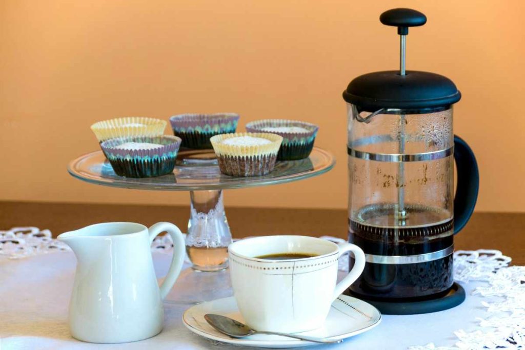 french press coffee maker next to pastries and a cup of coffee