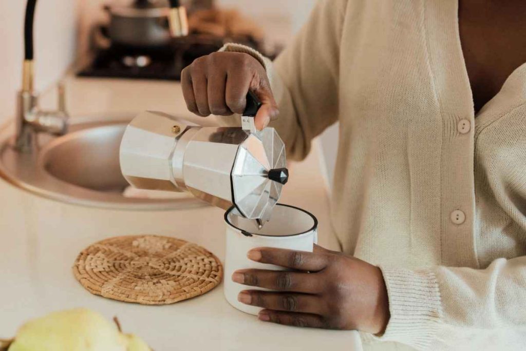 a woman pouring a cup of coffee from a moka pot