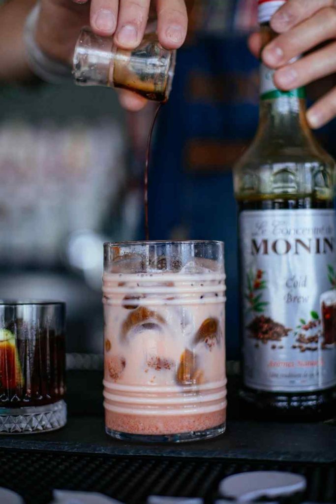 a hand pouring a shot of coffee syrup into a cold brew