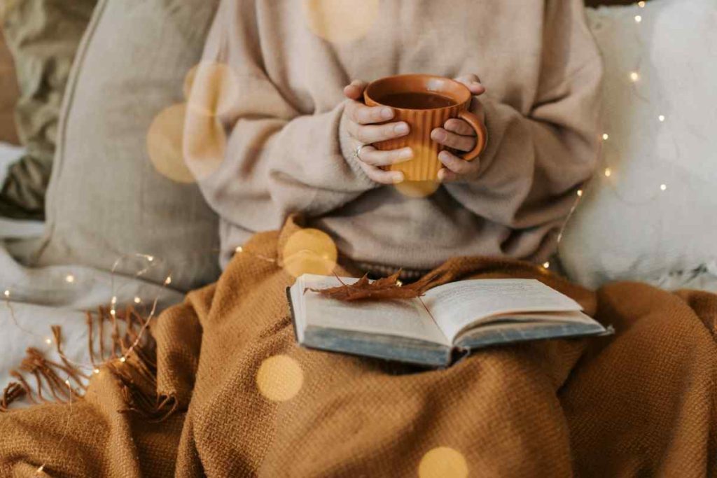 a hand holding a cup of coffee with an autumn blanket