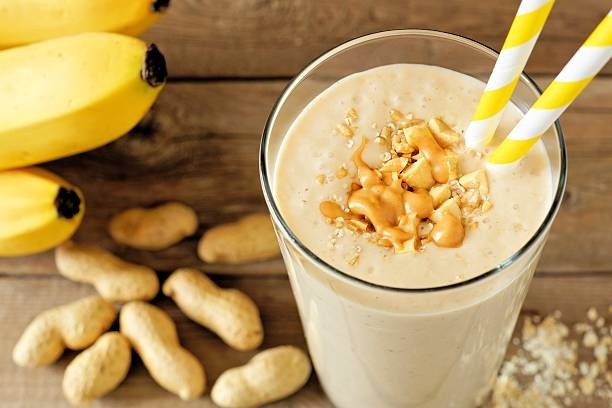 A glass of Peanut Butter Banana Espresso Shake smoothie with straws, peanut shells, and bananas