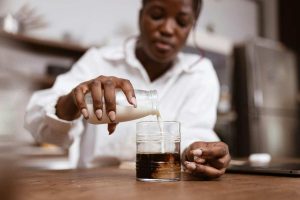 woman pouring milk into a glass of coffee