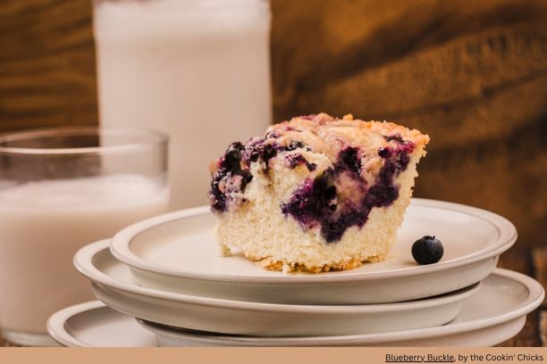 blueberry coffee cake on a stack of plates with a glass of milk in the background
