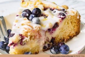 a bright yellow coffee cake topped with blueberries and white glaze on a plate
