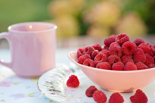 pink bowl of fresh raspberries next to a pink coffee cup